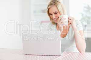 Close up of a woman holding coffee looking at the laptop in fron