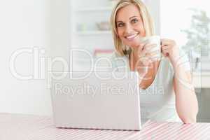 Close up of a woman holding coffee with laptop in front of her s