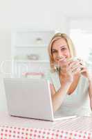 Close up of a woman holding cup of coffee with laptop in front o