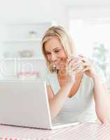Close up of a woman holding cup of coffee looking at laptop in f