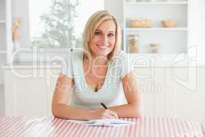 Woman sitting at a table writing a letter looking into camera