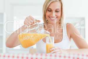 Close up of a smiling woman sitting at a table filling orange ju