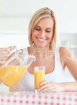 Close up of a smiling woman sitting at a table filling orange ju