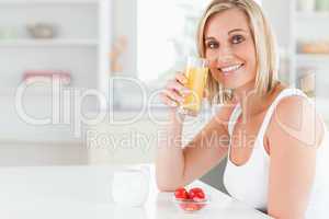 Woman sitting at a table toasting with orange juice looking into