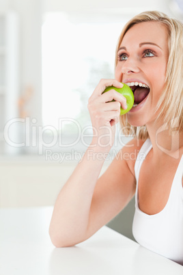 Young blonde woman sitting at table eating an apple