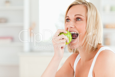 Young blonde woman sitting at table eating a green apple