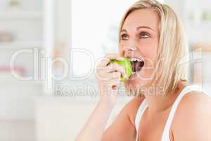 Young blonde woman sitting at table eating a green apple