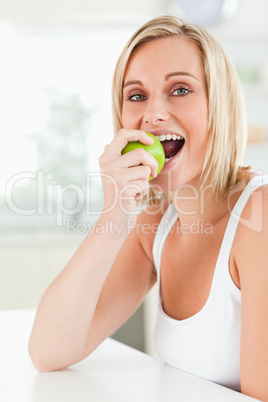 Young woman sitting at table eating a green apple while looking