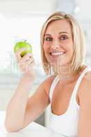 Young smiling woman holding a green apple looks into the camera