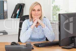 Smiling woman with chin on her hands behind a desk