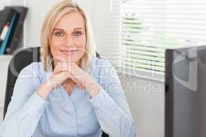 Cute blonde woman with chin on her hands behind a desk