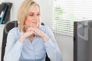 Cute blonde woman with chin on her hands behind a desk looking a
