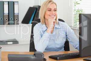 Smiling woman with chin on hand behind a desk looking at screen