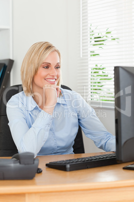 Smiling blonde woman with chin on hand behind a desk looking at
