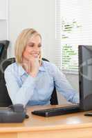 Smiling blonde woman with chin on hand behind a desk looking at