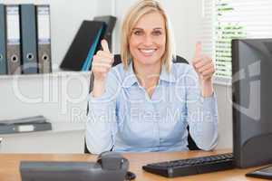 Young woman sitting behind desk with thumbs up