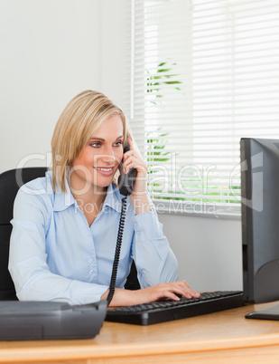 Smiling blonde businesswoman on the phone looking at her screen