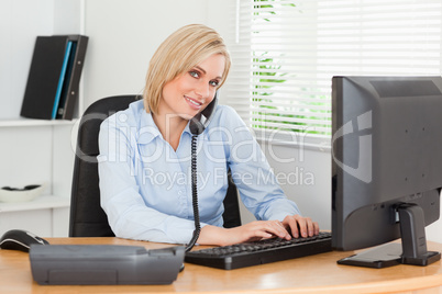 Working businesswoman on the phone while typing looks into camer