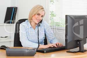 Working businesswoman on the phone while typing looks into camer