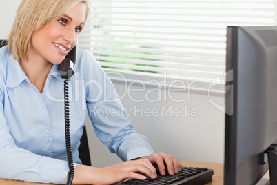 Smiling blonde businesswoman on the phone while typing looks at