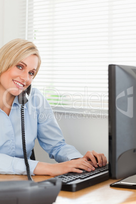 Charming blonde businesswoman on the phone while typing looks in