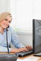 Charming blonde businesswoman on the phone while typing looks in