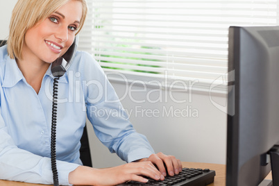 Smiling blonde businesswoman on the phone while typing looks int