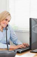 Charming blonde businesswoman on the phone while typing looks at
