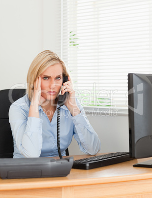 Blonde businesswoman on phone while having headache looks into c