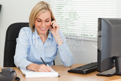 Cute blonde businesswoman on mobile writing something down