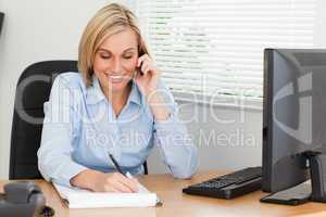 Cute blonde businesswoman on mobile writing something down