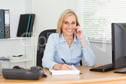 Cute businesswoman on mobile noting something looks into camera