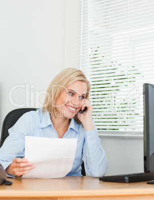 Businesswoman smiling at screen while phoning and holding a pape