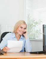 Businesswoman smiling at screen while phoning and holding a pape