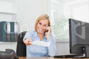 Businesswoman phoning and passing a paper looks into camera