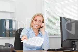 Smiling businesswoman phoning and passing a paper looks into cam