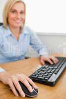 Blonde smiling businesswoman with hands on mouse and keyboard