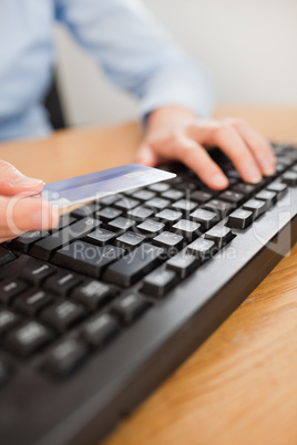 Woman typing on keyboard holding a card