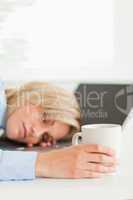 Gorgeous blonde woman sleeping on her laptop holding cup of coff