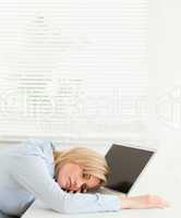 Cute blonde businesswoman sleeping on her notebook holding cup o