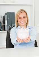 Cute blonde businesswoman holding a piggy bank
