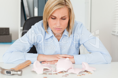 Sulking woman sitting in front of an shattered piggy bank with l