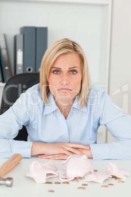 Sulking woman sitting in front of an shattered piggy bank lookin