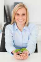 Smiling businesswoman holding a little green plant looking into