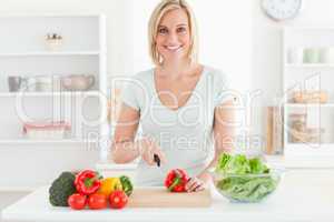 Young woman cutting vegetables smiles into camera