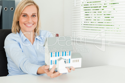 Gorgeous businesswoman presenting model house looks into camera