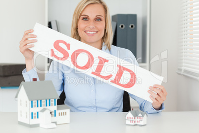 Blonde businesswoman showing SOLD sign looking into camera