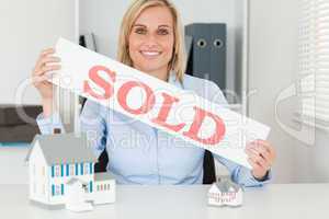 Blonde businesswoman showing SOLD sign looking into camera
