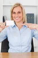 Smiling blonde businesswoman pointing at a card looks itno camer