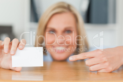 Businesswoman pointing at a card crouching behind her desk looks